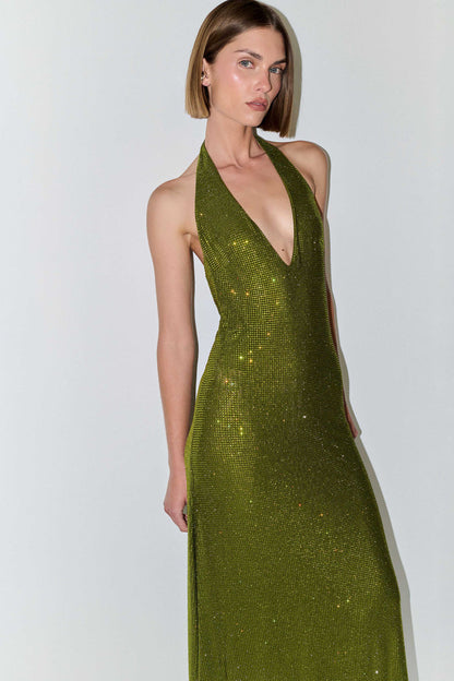 A woman modeling a sleeveless halter-neck maxi dress covered in shimmering olive green sequins against a plain light gray studio background.